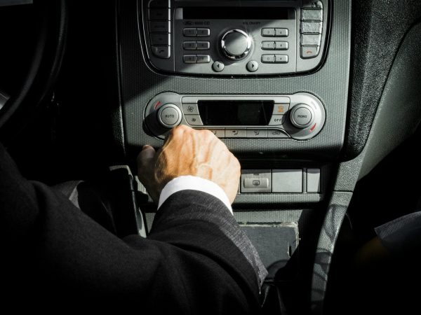 Close-up of a driver in a suit operating the car dashboard controls, capturing a professional interior setting.