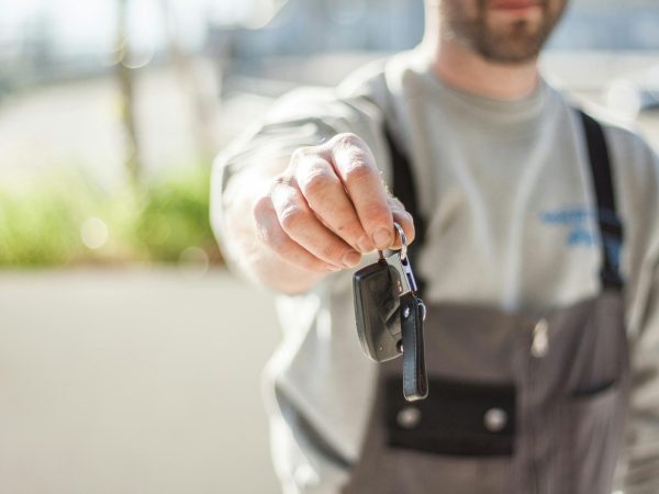 Hand holding a car key outdoors, blurred background, shallow focus.